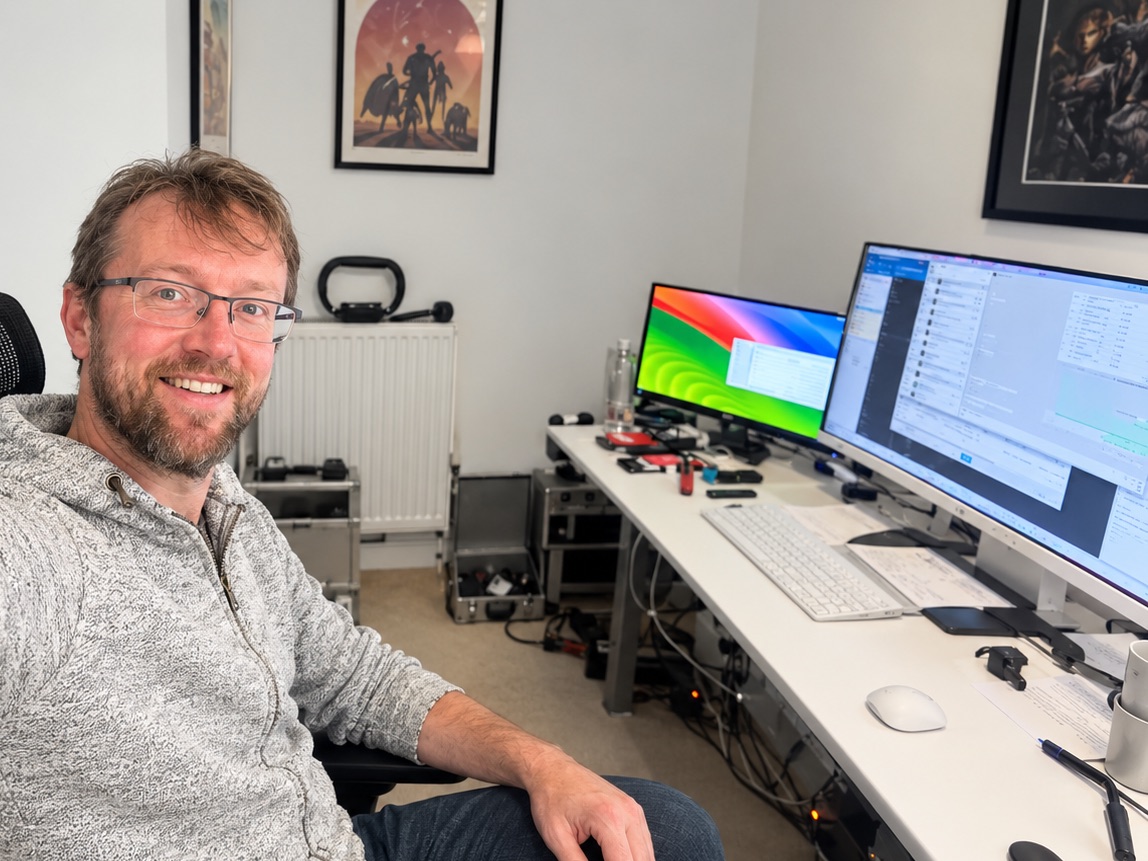 Ryan smiling at his desk in his home office, with his computer screens beside him